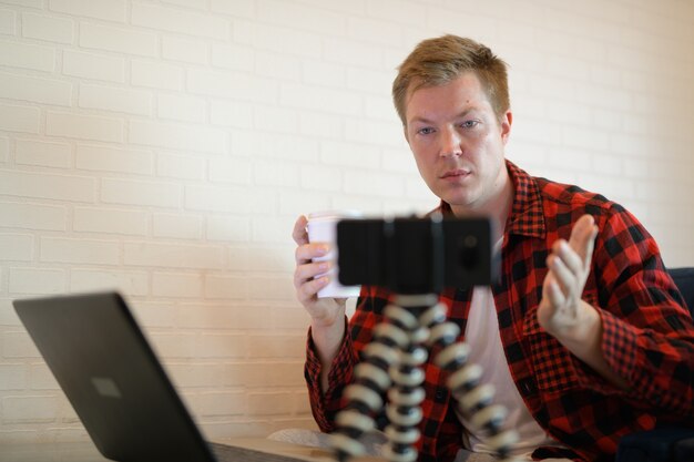 Jeune bel homme hipster buvant du café tout en vlogging au