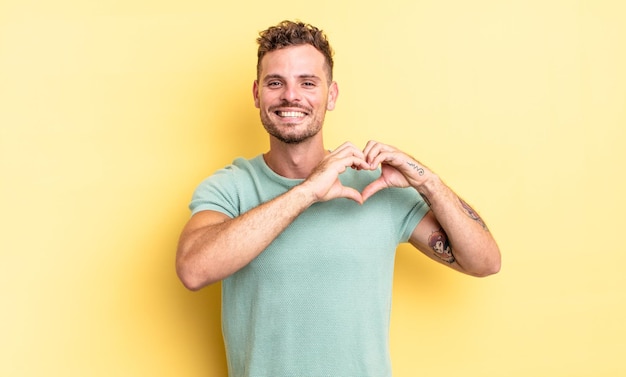 Jeune bel homme hispanique souriant et se sentant heureux, mignon, romantique et amoureux, faisant une forme de coeur avec les deux mains