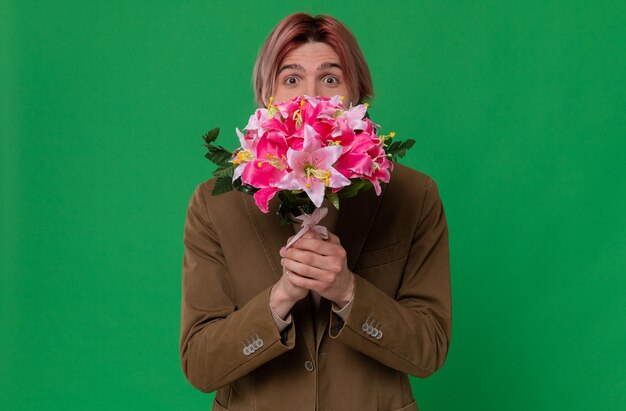 Jeune bel homme impressionné tenant le bouquet de fleurs et regardant