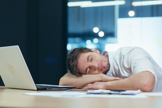 Jeune bel homme indépendant gestionnaire d'affaires au bureau à la table au repos s'est endormi dans ses bras à la table fatigué