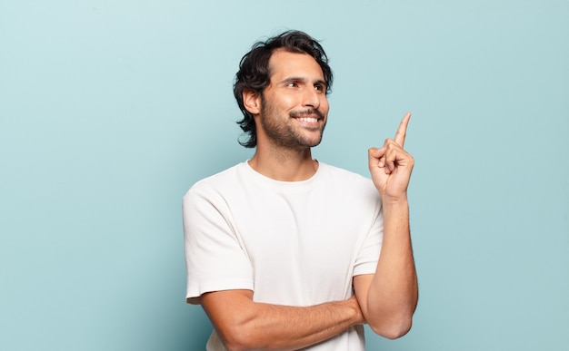 Jeune bel homme indien souriant joyeusement et regardant de côté, se demandant, pensant ou ayant une idée