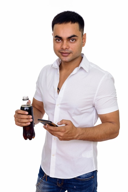 Jeune bel homme indien utilisant un téléphone mobile tout en tenant une bouteille de soda