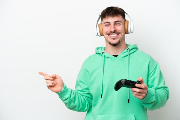 Jeune bel homme jouant avec un contrôleur de jeu vidéo isolé sur fond blanc pointant le doigt sur le côté