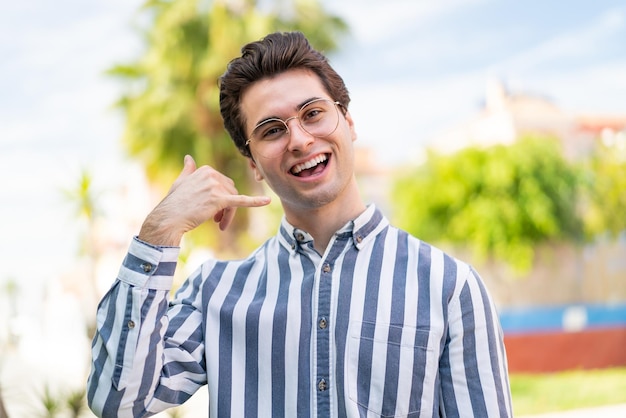 Jeune bel homme avec des lunettes et faisant un geste de téléphone