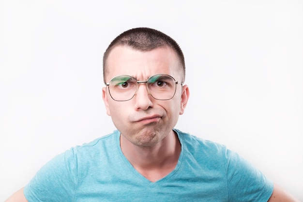 Jeune bel homme à lunettes pensant dans les doutes et touchant les lèvres sur gris