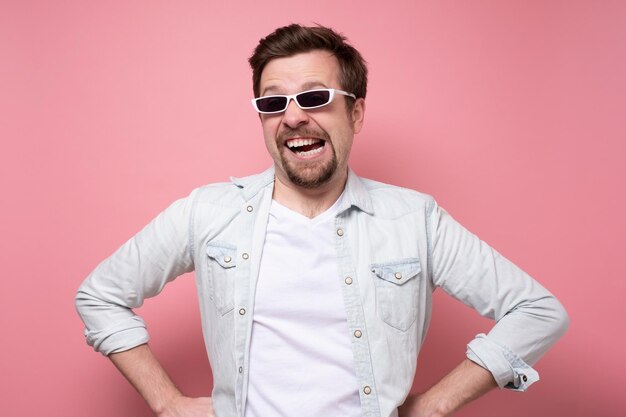 Jeune bel homme à lunettes de soleil souriant sur un mur rose