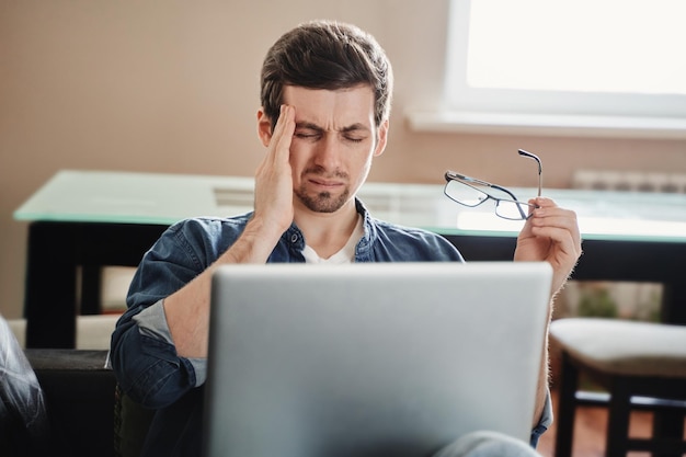 Jeune bel homme a mal à la tête à cause du surmenage sur ordinateur