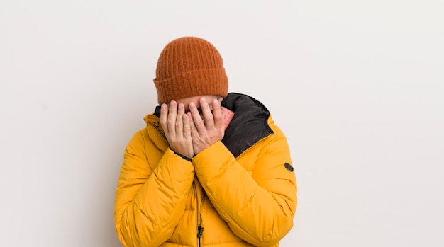 Jeune bel homme avec un manteau contre un mur blanc