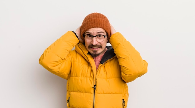 Jeune bel homme avec un manteau contre un mur blanc