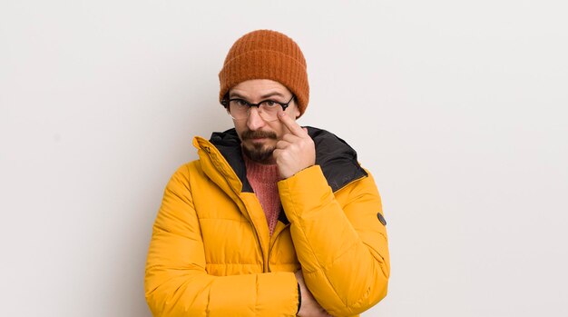 Jeune bel homme avec un manteau contre un mur blanc