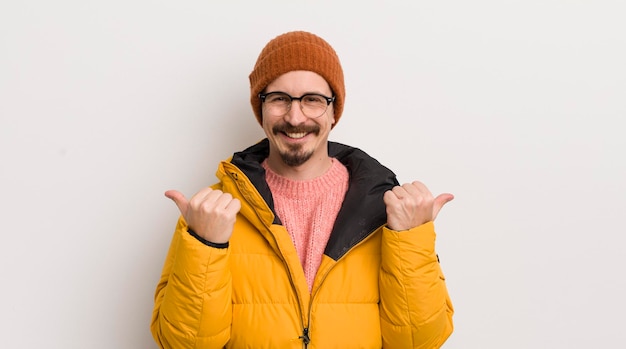 Jeune bel homme avec un manteau contre un mur blanc