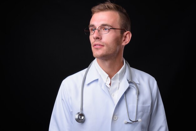 Jeune bel homme médecin aux cheveux blonds contre le mur noir