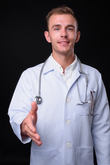 Jeune bel homme médecin aux cheveux blonds contre le mur noir