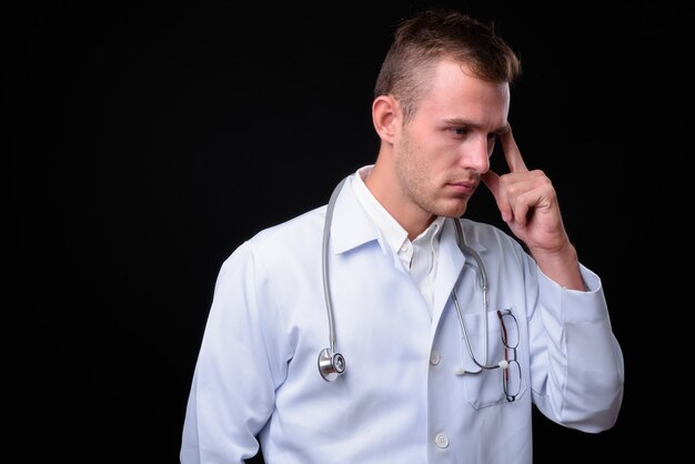 Jeune bel homme médecin aux cheveux blonds contre le mur noir