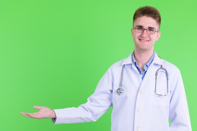 Jeune bel homme médecin avec des lunettes contre la clé de chrominance avec mur vert