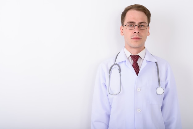 Jeune bel homme médecin portant des lunettes sur un mur blanc