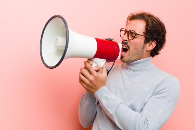 Jeune bel homme avec un mégaphone sur mur plat rose