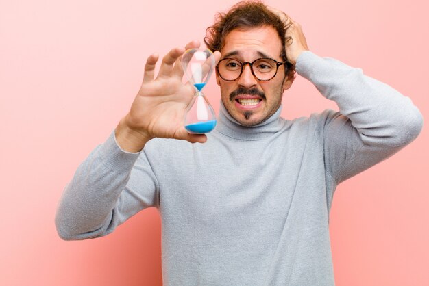 Jeune bel homme avec une minuterie de sable contre le mur plat rose