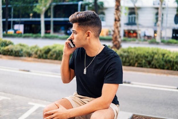 Jeune bel homme à la mode dans la rue de la ville moderne parlant sur un téléphone portable. Notion de communication