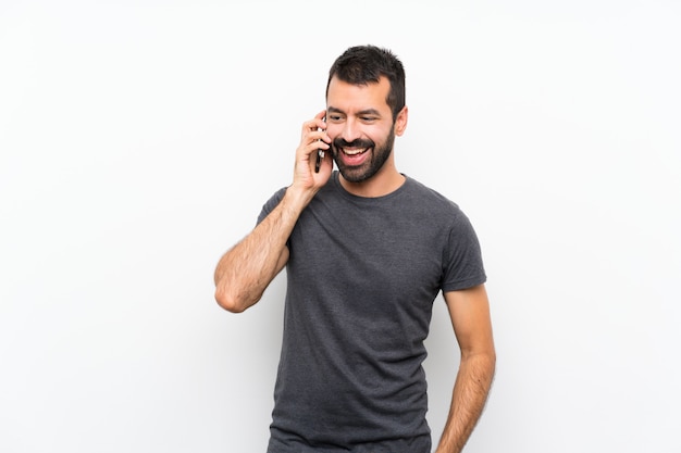 Jeune bel homme sur un mur blanc isolé, gardant une conversation avec le téléphone mobile