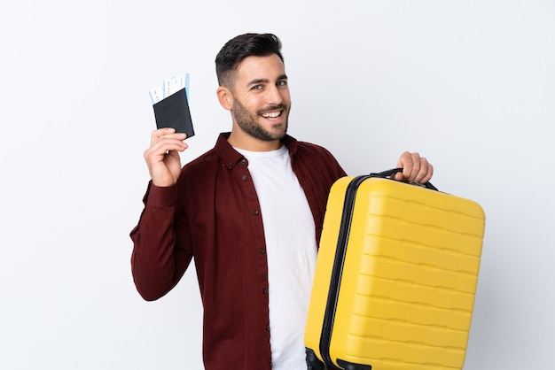 Jeune bel homme sur un mur blanc isolé en vacances avec valise et passeport