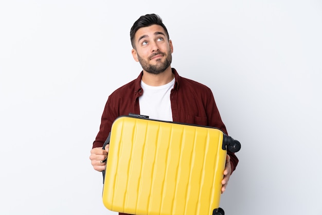 Jeune bel homme sur un mur blanc isolé en vacances avec valise de voyage