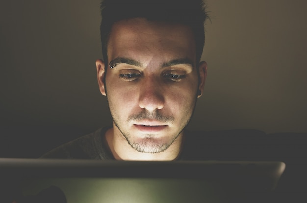 Jeune bel homme à un ordinateur portable avec réflexion de la lumière de l'écran au visage - concept de technologie, internet et personnes