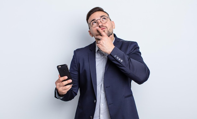 Jeune bel homme pensant, se sentant douteux et confus et concept d'entreprise et de smartphone