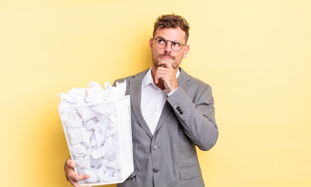 Jeune bel homme pensant, se sentant douteux et confus concept de poubelle de boules de papier