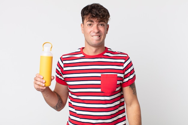 Jeune bel homme à la perplexité et confus et tenant un thermos de café