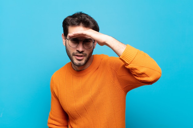 Jeune bel homme à la perplexité et étonné, avec la main sur le front à la recherche de loin, regarder ou chercher