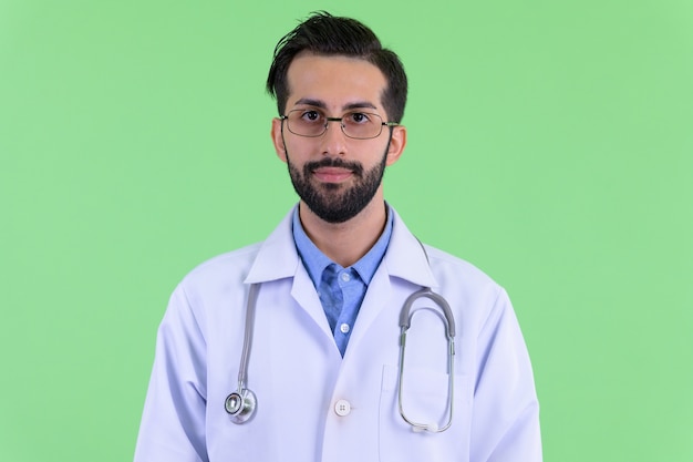 Jeune bel homme persan barbu médecin contre le mur vert