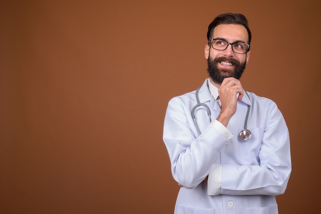 Jeune bel homme persan barbu médecin sur mur marron