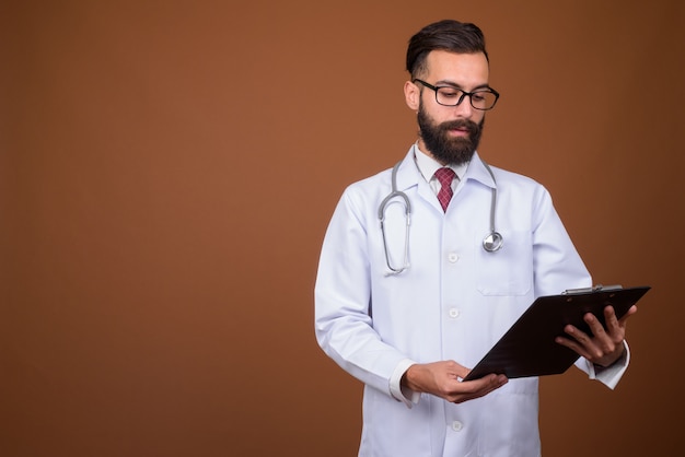 Jeune bel homme persan barbu médecin sur mur marron