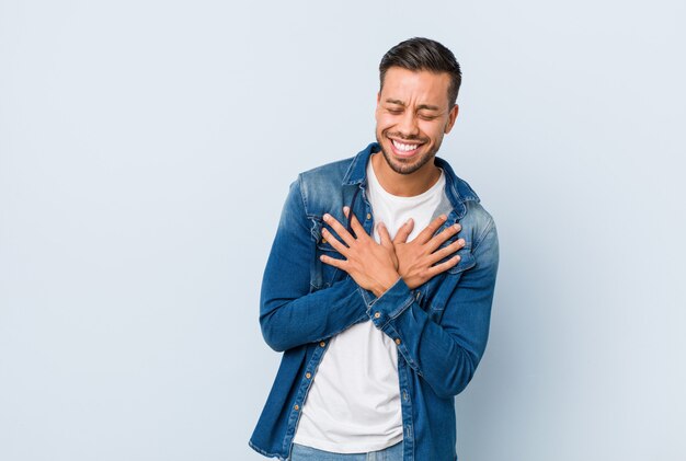 Jeune bel homme philippin rire gardant les mains sur le coeur, concept de bonheur.