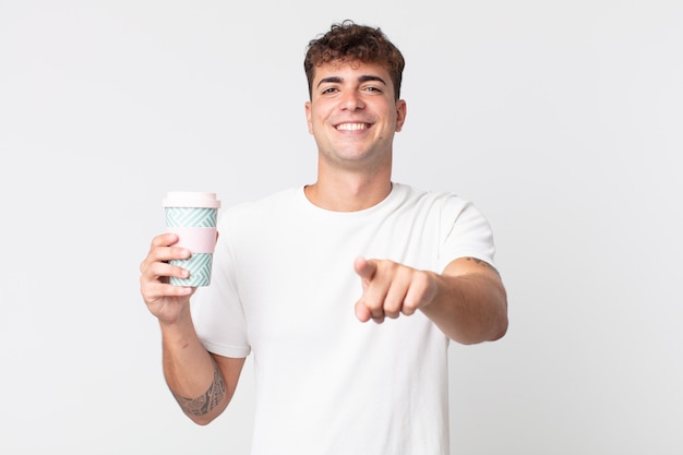 Jeune bel homme pointant sur la caméra vous choisissant et tenant un café à emporter