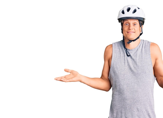 Jeune bel homme portant un casque de vélo expression désemparée et confuse avec les bras et les mains soulevées concept de doute