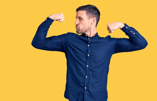 Jeune bel homme portant une chemise décontractée montrant les muscles des bras souriant fier concept de remise en forme