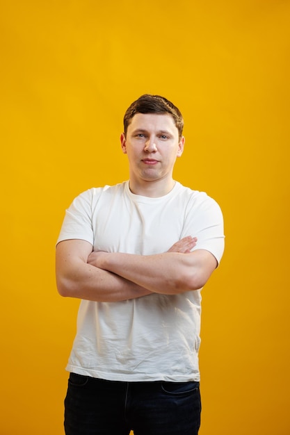 Jeune bel homme portant un t-shirt blanc avec un visage heureux souriant avec les bras croisés en regardant la caméra sur fond de studio jaune Personne positive