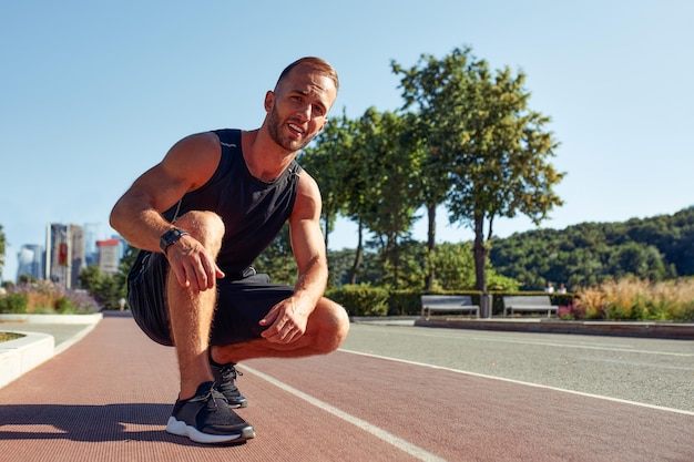 Jeune bel homme en position de départ pour courir sur une piste de sport