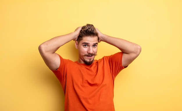 Jeune bel homme qui a l'air excité et surpris, la bouche ouverte avec les deux mains sur la tête, se sentant comme un heureux gagnant. étrange concept de moustache