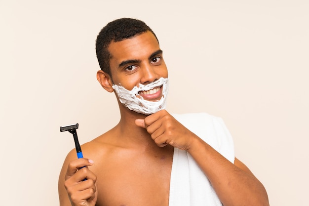 Jeune bel homme rasant sa barbe sur le mur, pensant à une idée et regardant de côté