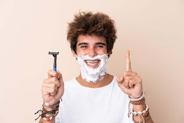 Jeune bel homme rasant sa barbe pointant vers le haut une excellente idée