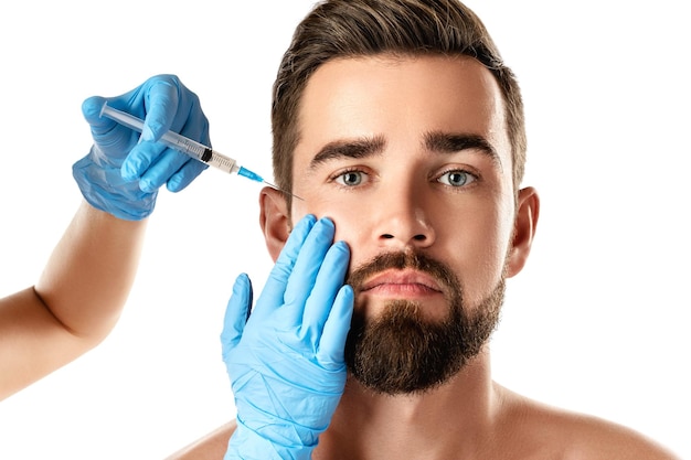 Jeune bel homme recevant une injection faciale pour le rajeunissement de la peau sur fond blanc