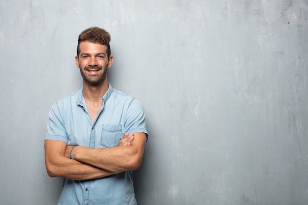 Jeune bel homme avec un regard fier, satisfait et heureux sur le visage, souriant avec les bras croisés