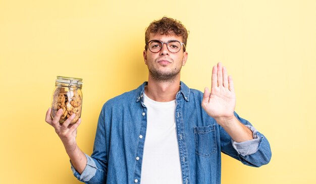 jeune bel homme regardant sérieux montrant la paume ouverte faisant un geste d'arrêt. concept de bouteille de biscuits