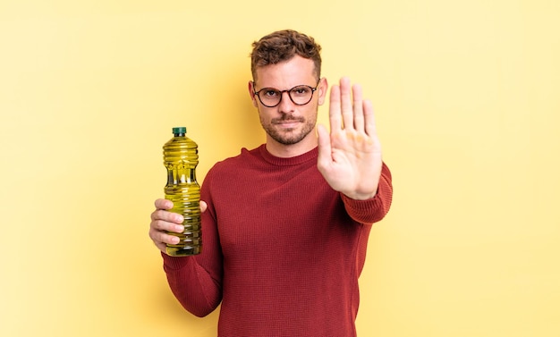 Jeune bel homme regardant sérieux montrant la paume ouverte faisant un geste d'arrêt. concept d'huile d'olive