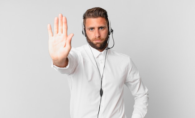 jeune bel homme regardant sérieux montrant la paume ouverte faisant un geste d'arrêt. concept de télémarketing