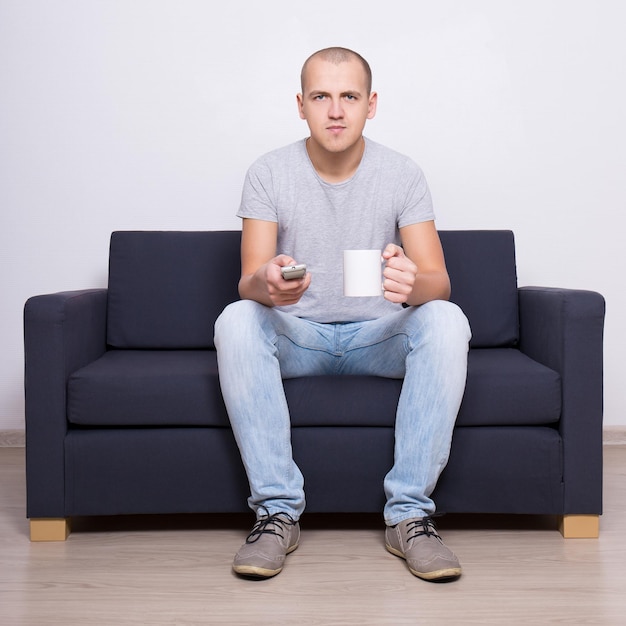 Jeune bel homme regardant la télévision avec une tasse de thé ou de café