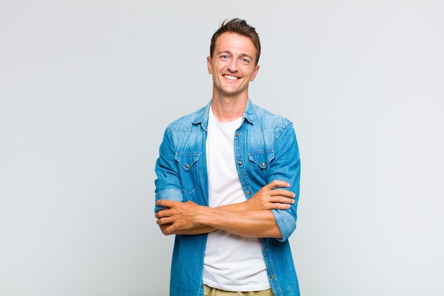 Jeune bel homme ressemblant à un réalisateur heureux, fier et satisfait souriant, les bras croisés
